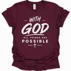 A maroon short-sleeve crewneck t-shirt with a white graphic text print reading 'WITH GOD ALL THINGS ARE POSSIBLE' and a cross symbol, shown on a plain white background.