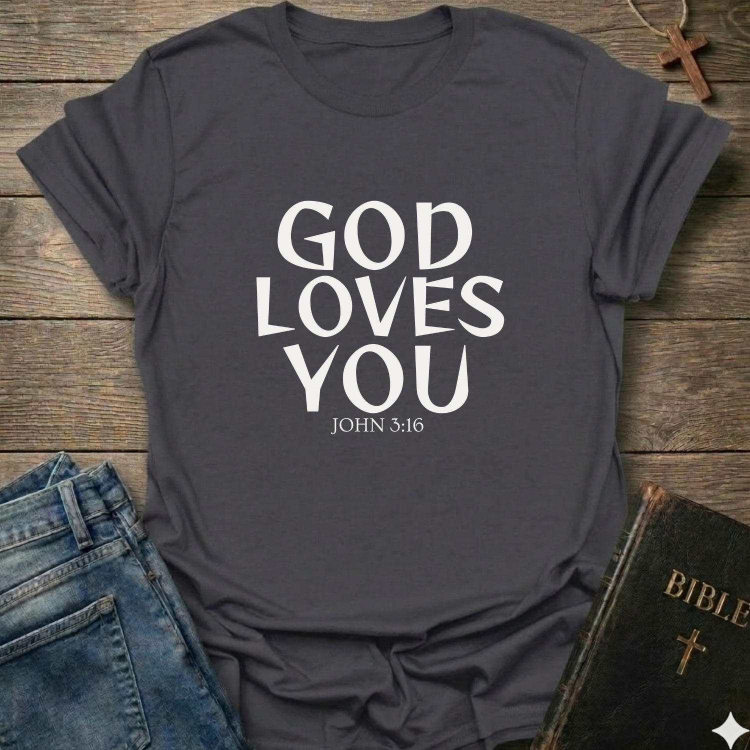 Heather Grey t-shirt with 'GOD LOVES YOU' John 3:16 text Christian bold faith apparel Faith Forward on a wooden surface with jeans and a Bible.