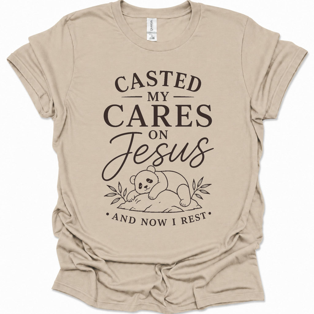 A sand colored short-sleeve t-shirt with a black graphic print that reads 'CASTED MY CARES ON Jesus AND NOW I REST' with a cartoon bear illustration, shown on a plain white background.