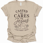 A sand colored short-sleeve t-shirt with a black graphic print that reads 'CASTED MY CARES ON Jesus AND NOW I REST' with a cartoon bear illustration, shown on a plain white background.