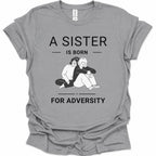 A sport gray short-sleeve t-shirt with a black graphic print that reads 'A SISTER IS BORN FOR ADVERSITY' surrounding an illustration of two people hugging. The Gildan brand tag is visible inside the collar.