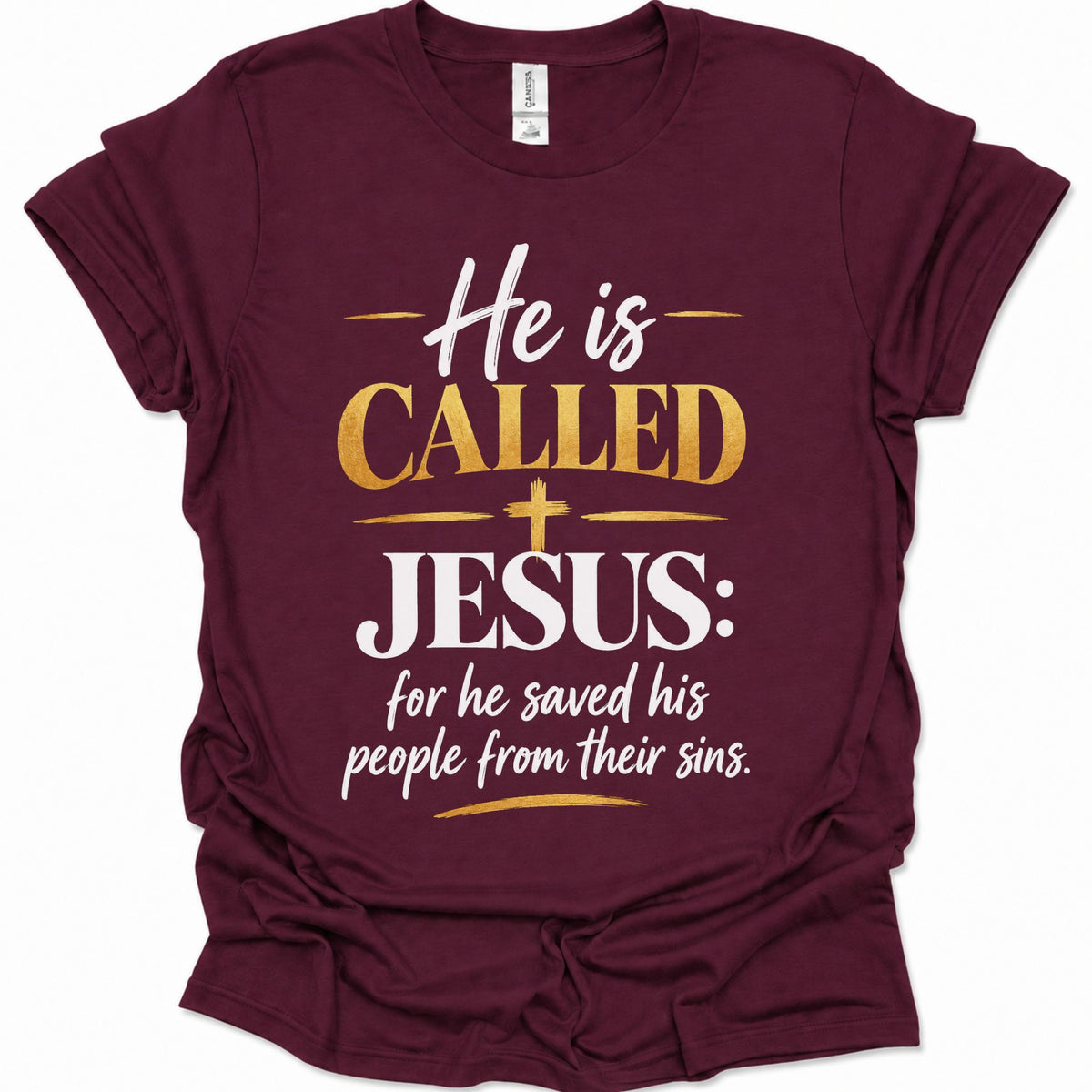 A maroon short-sleeve t-shirt with a graphic print on the front that reads 'He is CALLED JESUS: for he saved his people from their sins.' in white and gold lettering, displayed on a clean white background.
