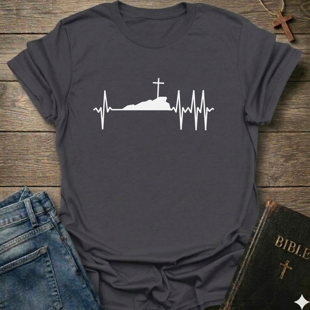 Dark gray T-shirt with a white graphic design Cross Heartbeat Lifeline Christian minimal faith apparel conversation starter on a wooden surface with jeans and a Bible.