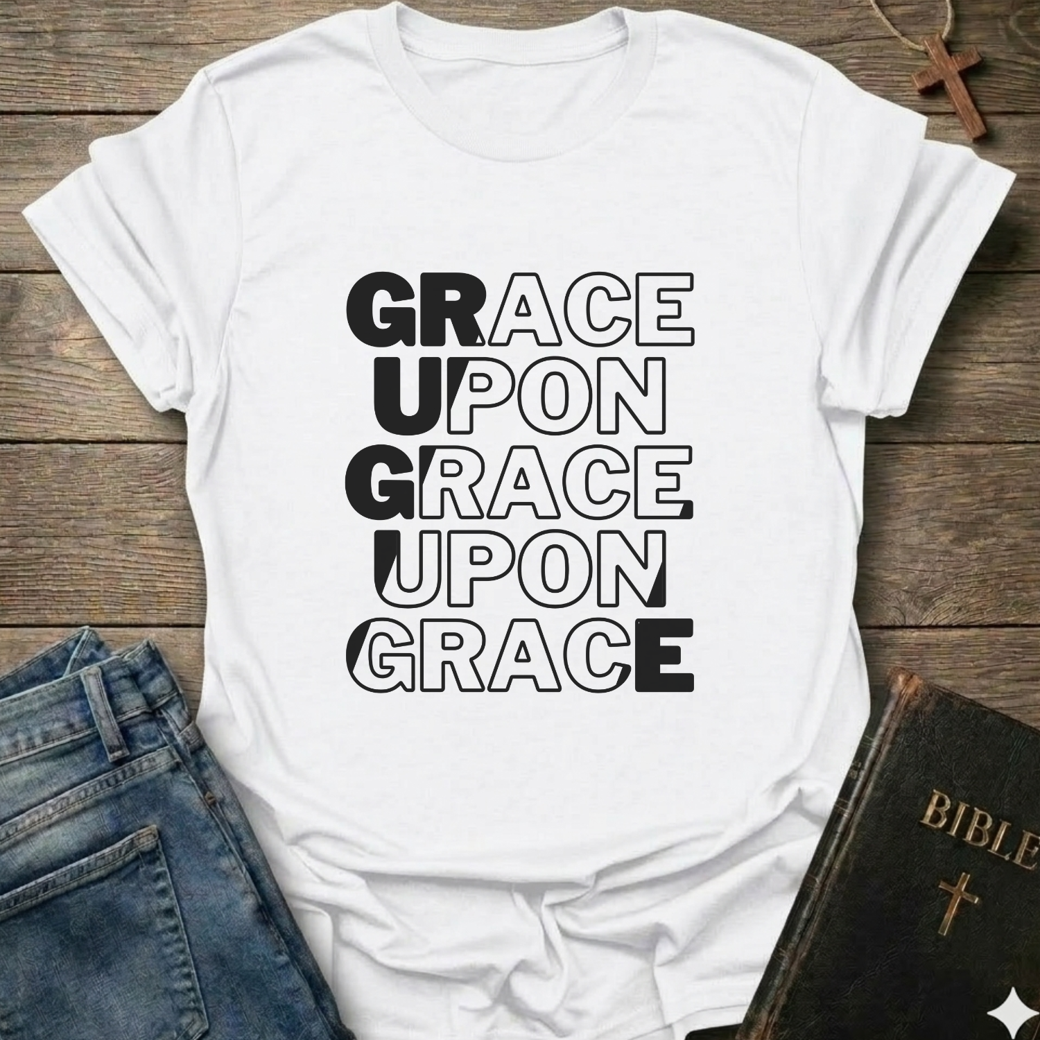 White t-shirt with 'Grace Upon Grace Upon Grace' Christian T-Shirt John 1:16 bold faith apparel text on a wooden surface with jeans and a Bible.