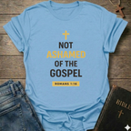 Light blue t-shirt with 'Not Ashamed of the Gospel' text on a wooden surface with a Bible and cross. Christian T-Shirt Romans 1:16 bold faith apparel Faith Forward