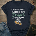 Black t-shirt Casted My Cares on Jesus Christian relatable faith apparel conversation starter with a panda graphic and text on a wooden surface with jeans and a Bible.