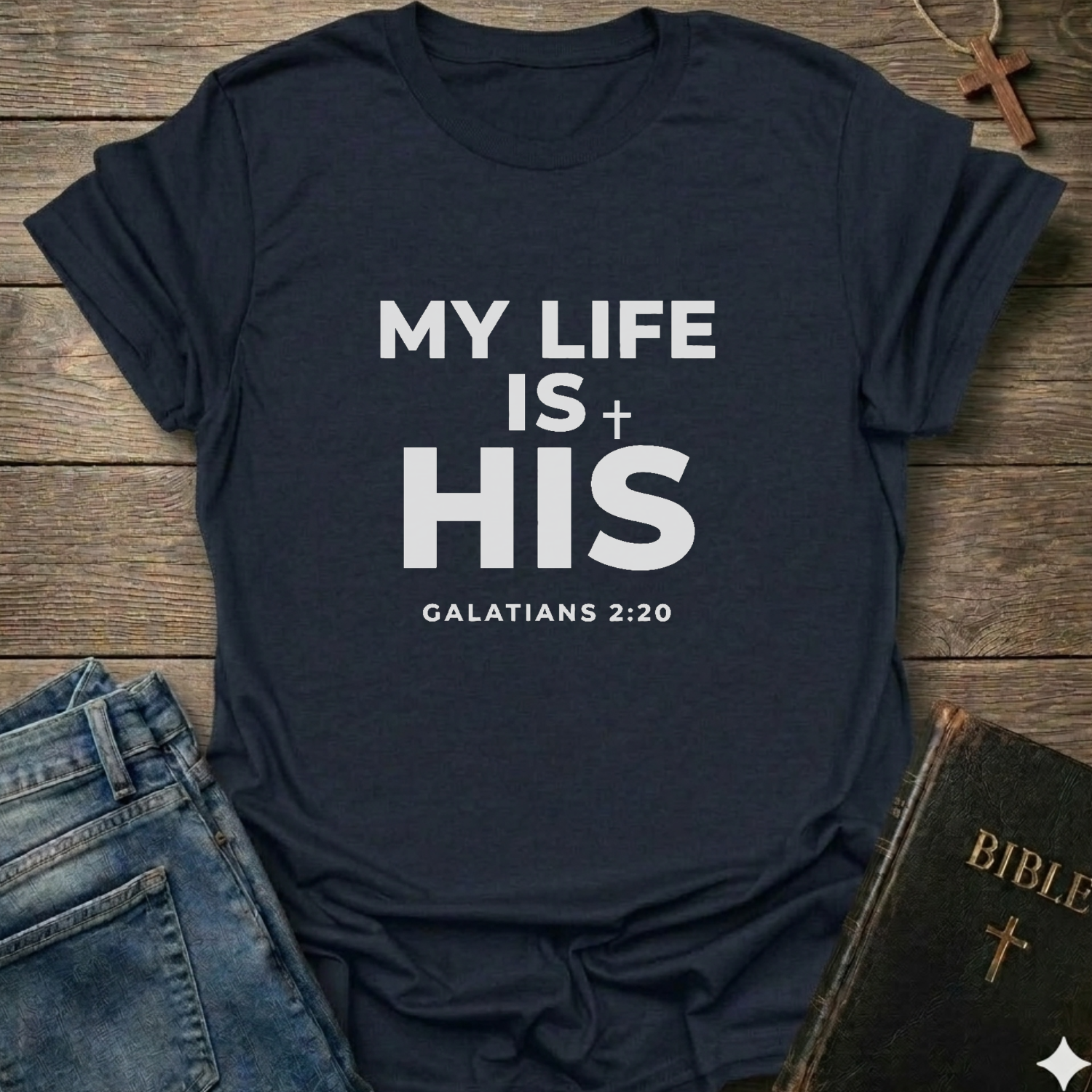 Navy blue t-shirt with 'My Life Is His'  Christian T-Shirt Galatians 2:20 bold faith apparel Faith Forward text on a wooden surface with jeans and a Bible.