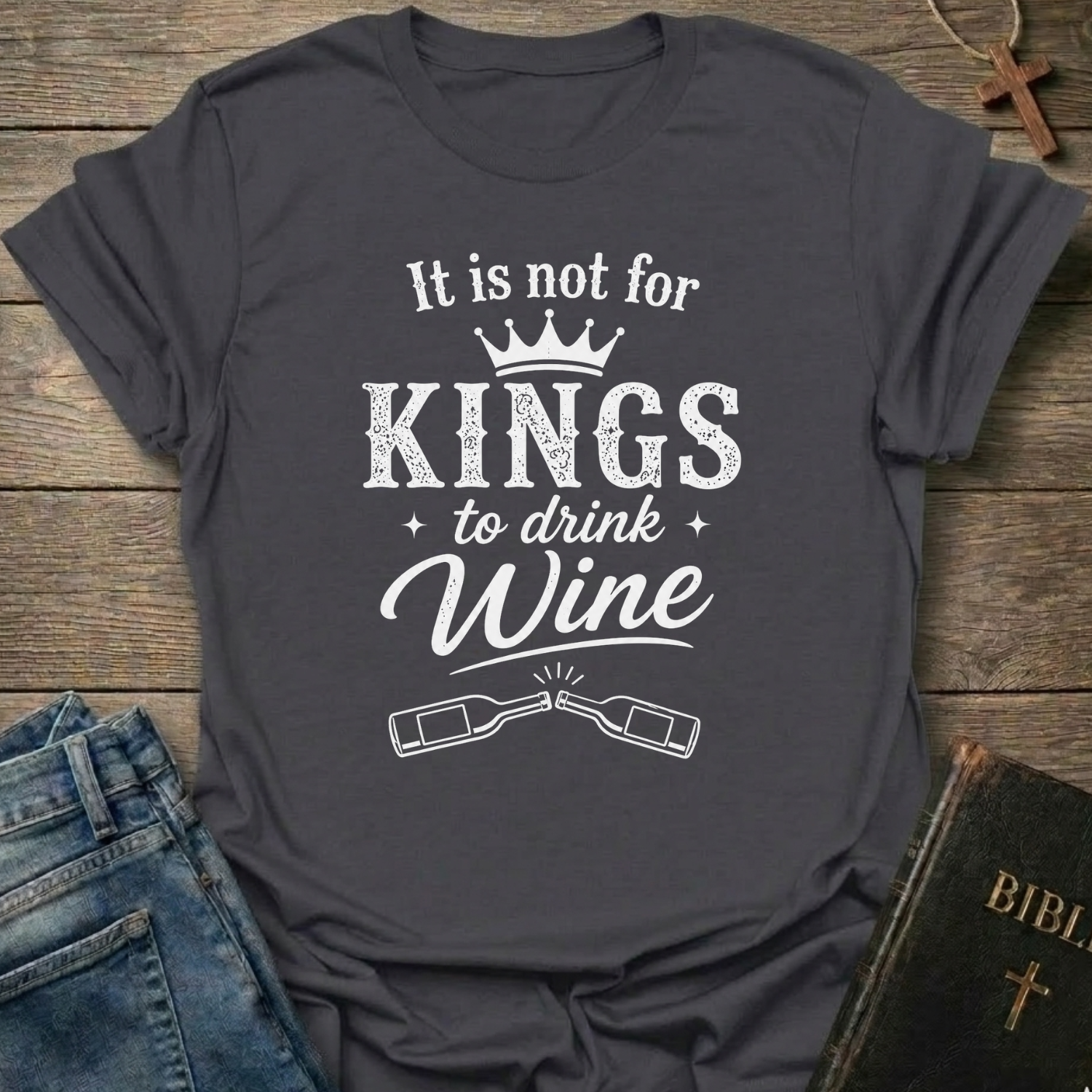 Gray t-shirt with white text "It is Not for Kings to Drink Wine" and 2 wine bottles graphic based on Proverbs 31:4 Christian faith apparel conversation starter on a wooden surface with jeans and a Bible.