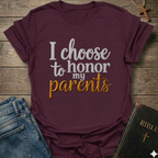 Maroon t-shirt with 'I choose to honor my parents' Exodus 20:12 text navy gold Christian faith apparel conversation starter. T-shirt is on a wooden surface with jeans and a Bible.