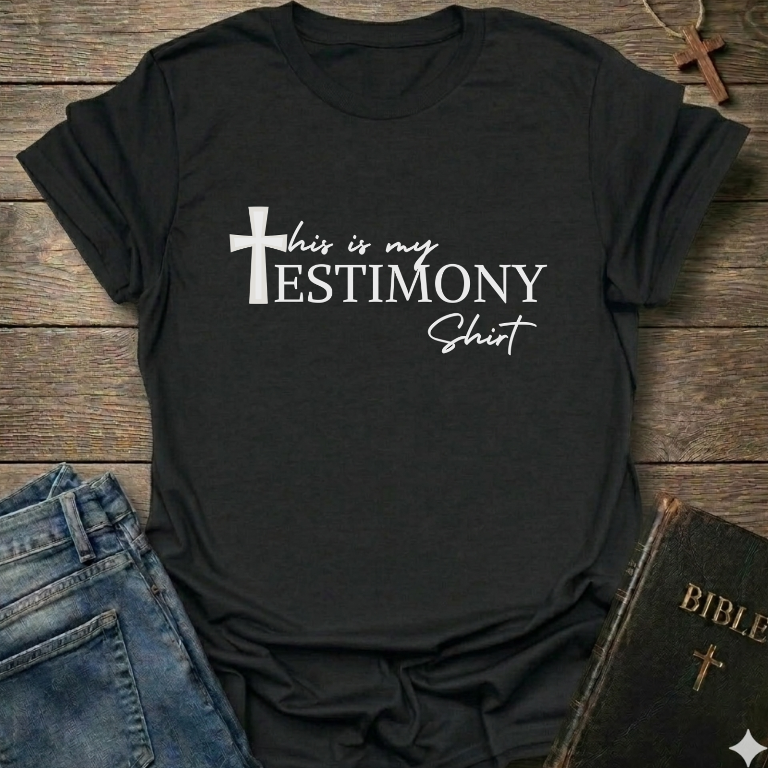 Black t-shirt with 'This is my testimony shirt' text and cross minimal faith apparel conversation starter. It is on a wooden surface with jeans and a Bible.