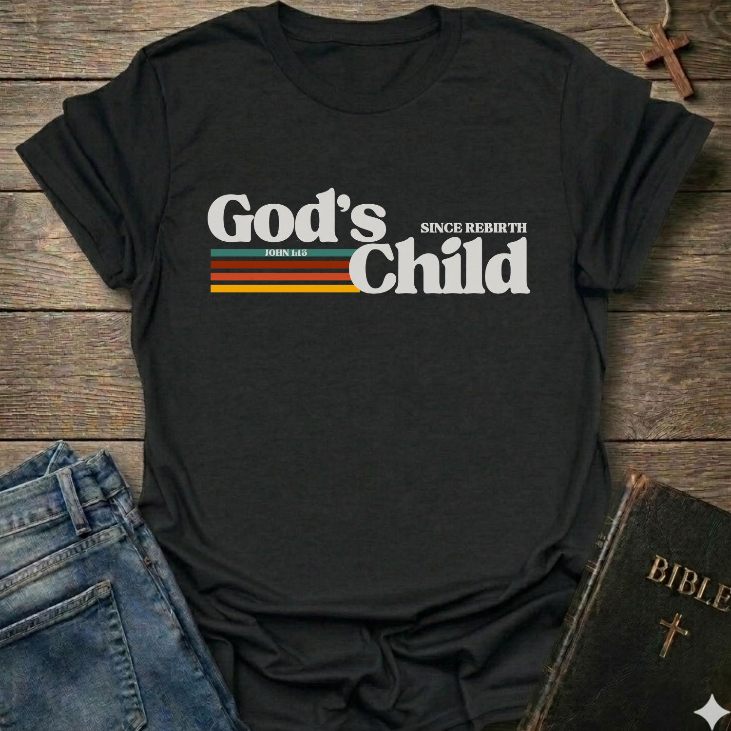 Black t-shirt with God's Child Since Rebirth Christian T-Shirt John 1:12 retro faith apparel conversation starter text on a wooden surface with jeans and a Bible.