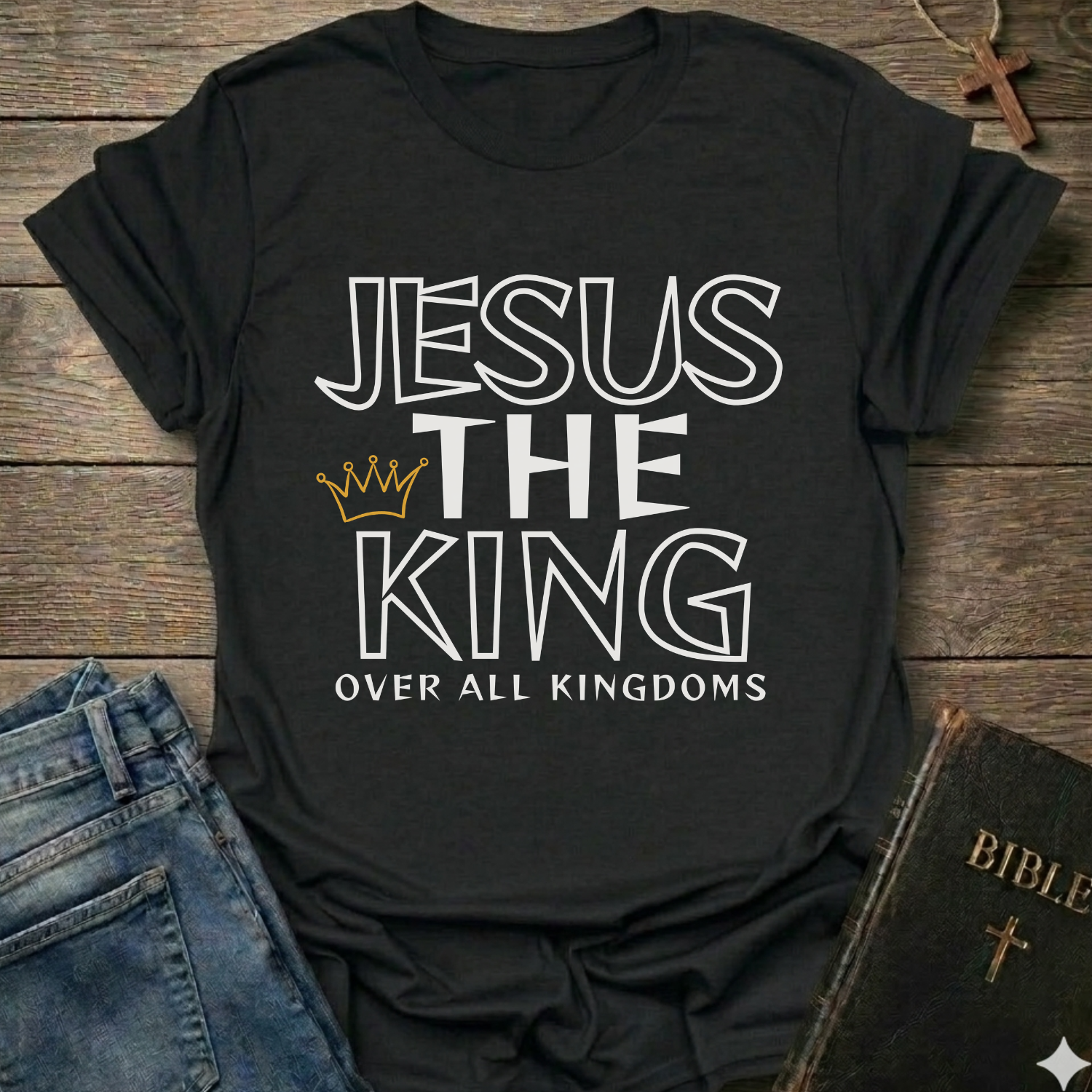 Black t-shirt with text 'Jesus The King Over All Kingdoms'  and crown Christian bold faith apparel Faith Forward text on a wooden surface with jeans and a Bible.