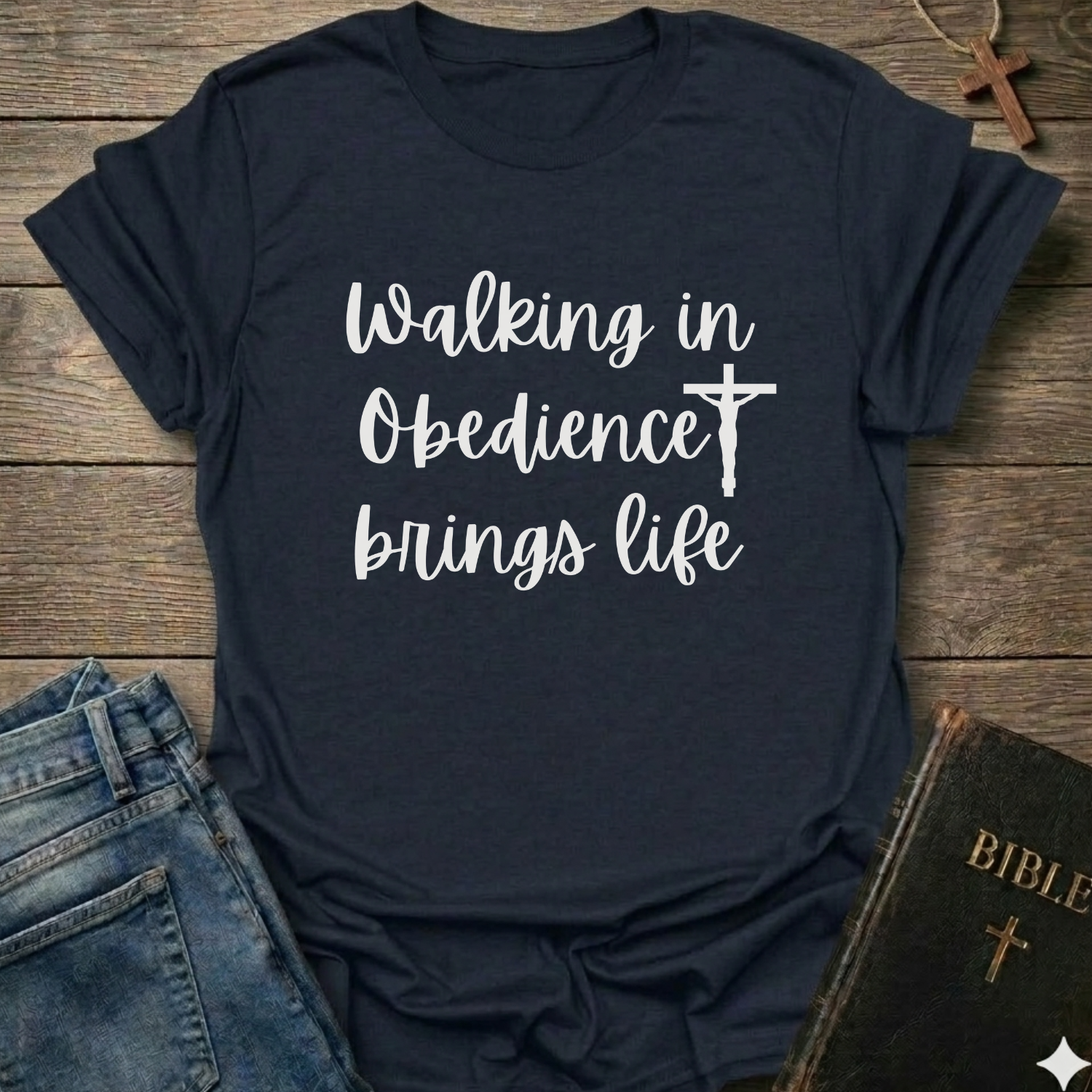 Navy blue t-shirt with 'Walking in Obedience brings life' text and cross graphic Christian script faith apparel conversation starter on a wooden surface.