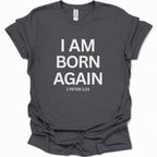 A dark heather gray short-sleeve t-shirt with bold white text reading 'I AM BORN AGAIN' and '1 PETER 1:23' printed on the front, shown on a plain white background.