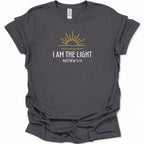A dark heather gray short-sleeve t-shirt with a graphic print of a yellow rising sun and the text 'I AM THE LIGHT MATTHEW 5:14' in white and yellow, displayed on a clean white background.