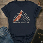 Navy blue Christian t-shirt with 'Faith can move mountains' graphic Matthew 17:20 faith apparel conversation starter on a wooden surface with jeans and a Bible. surface.