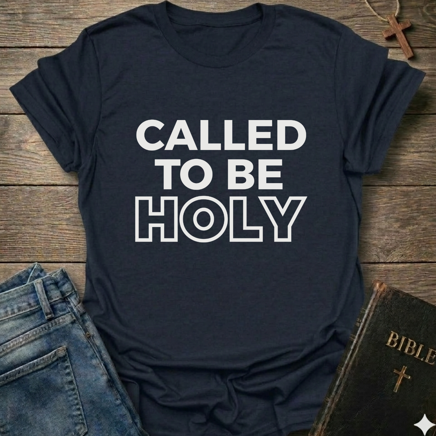 Navy Blue t-shirt with 'Called to be Holy' Christian T-Shirt bold faith apparel 1 Peter 1:15 conversation starter text on a wooden surface with jeans and a Bible.