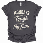 A dark heather gray short-sleeve t-shirt with a distressed cream-colored graphic text that reads 'MONDAYS are Tough so is My Faith'. The t-shirt is displayed flat against a clean white background.