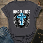 Gray Christian T-Shirt with lion graphic and 'King of Kings' text Revelation 19:16 bold faith apparel conversation starter on a wooden surface with jeans and a Bible.