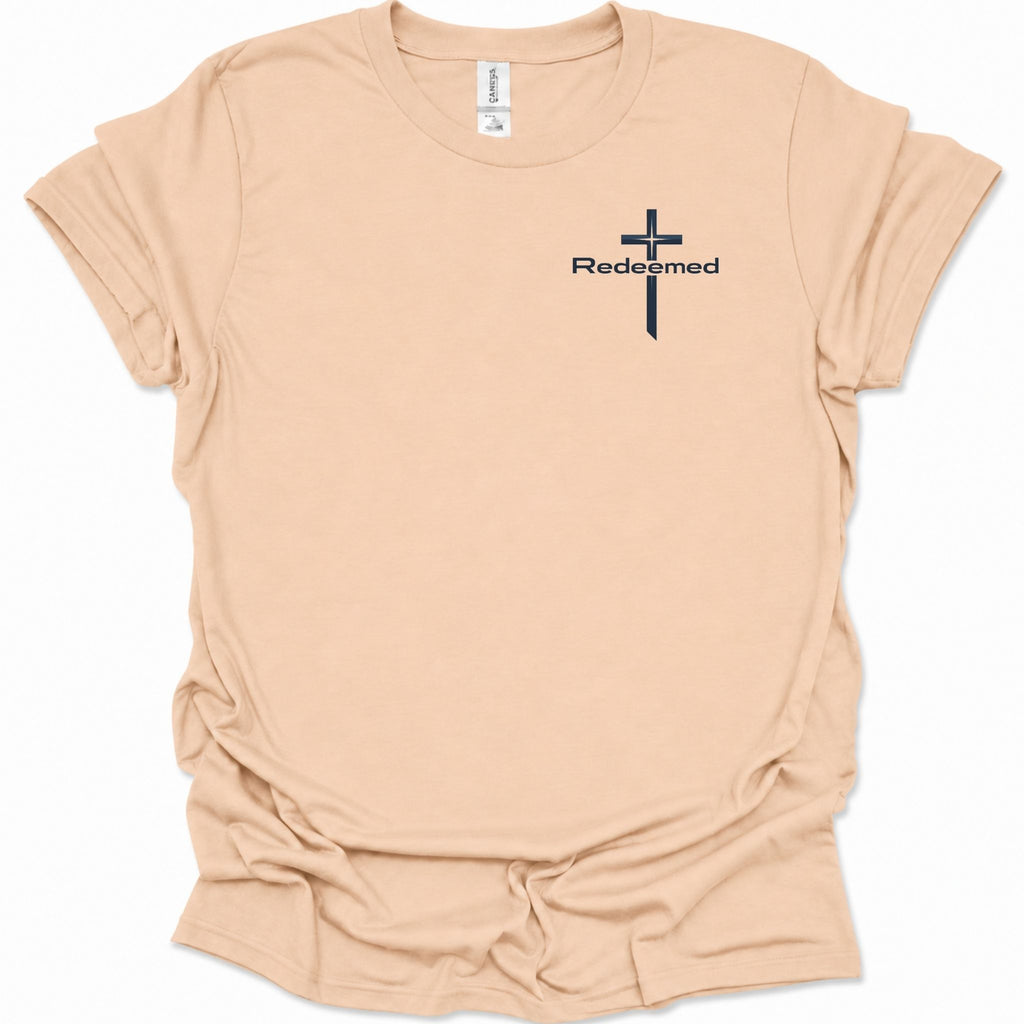 A light natural-colored short-sleeve t-shirt with a black cross graphic and the word 'Redeemed' printed on the left chest, displayed on a clean white background.