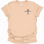 A light natural-colored short-sleeve t-shirt with a black cross graphic and the word 'Redeemed' printed on the left chest, displayed on a clean white background.