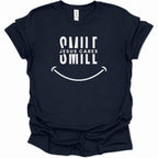 A navy blue short-sleeve t-shirt with a white graphic print on the front that reads 'SMILE JESUS CARES SMILL' above a smiley face, shown on a plain white background.
