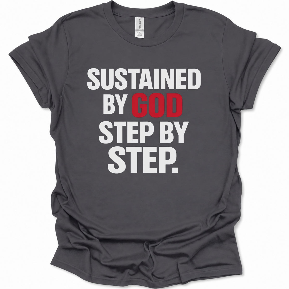A dark heather gray short-sleeve t-shirt with a graphic text print reading 'SUSTAINED BY GOD STEP BY STEP.' in white and red lettering, displayed on a clean white background.