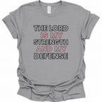 A sport gray short-sleeve crewneck t-shirt with a graphic text print reading 'THE LORD IS MY STRENGTH AND MY DEFENSE' in black and red lettering, laid flat on a white background.
