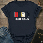 Black t-shirt with 'Need Jesus' graphic on a wooden surface with jeans and a Bible. Need Jesus to Recharge My Battery Christian T-Shirt bold faith apparel Faith Forward