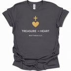 A dark heather gray short-sleeve t-shirt with a graphic on the front featuring a gold heart and cross, the text 'TREASURE -> HEART', and 'MATTHEW 6:21' in white, shown on a plain white background.