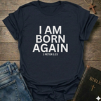 Navy blue t-shirt with 'I AM BORN AGAIN 1 PETER 1:23' text I Am Born Again Christian bold faith apparel conversation starter on a wooden surface with jeans and a Bible.