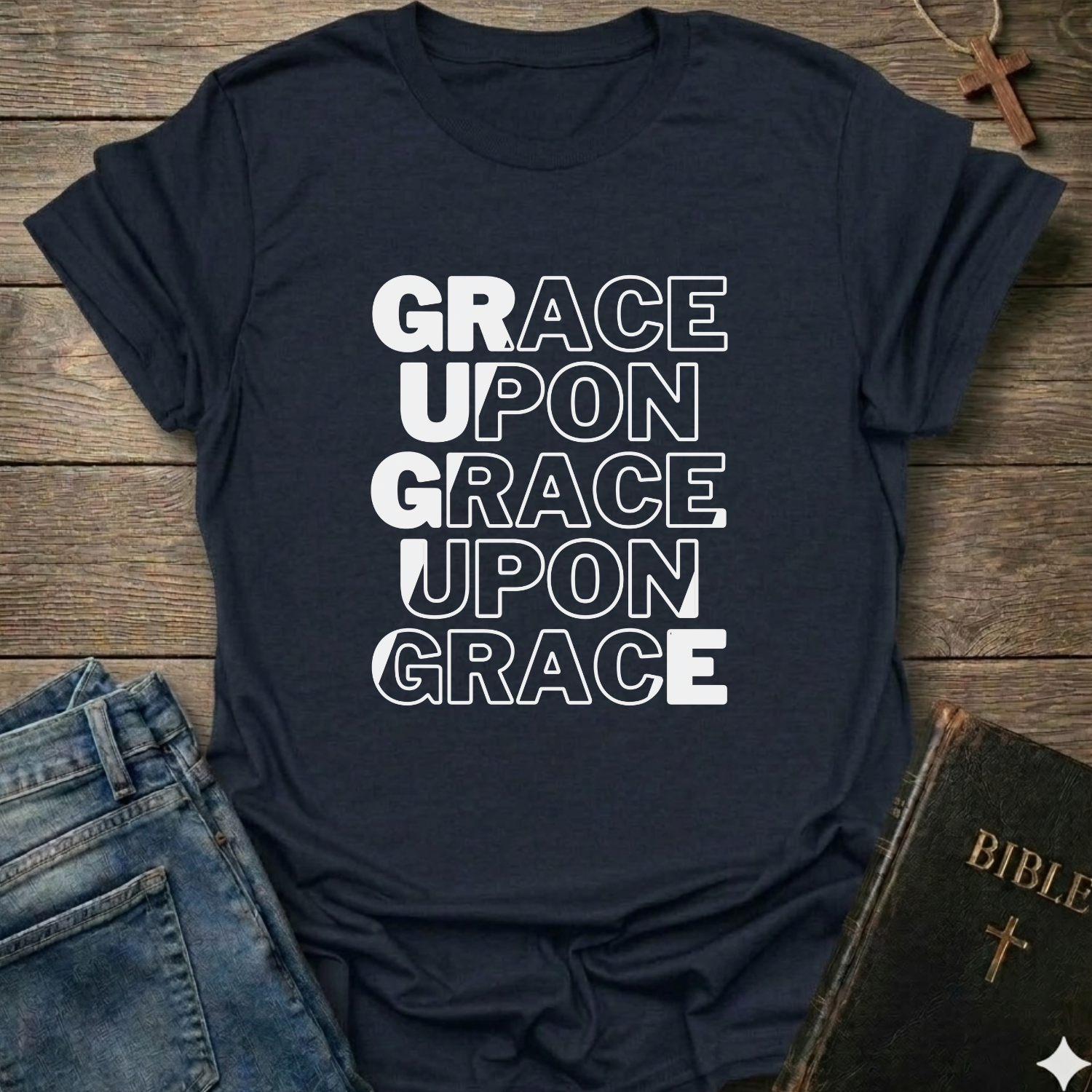 Navy blue t-shirt with 'GRACE UPON GRACE' Christian T-Shirt John 1:16 bold faith apparel text on a wooden surface with jeans and a Bible.