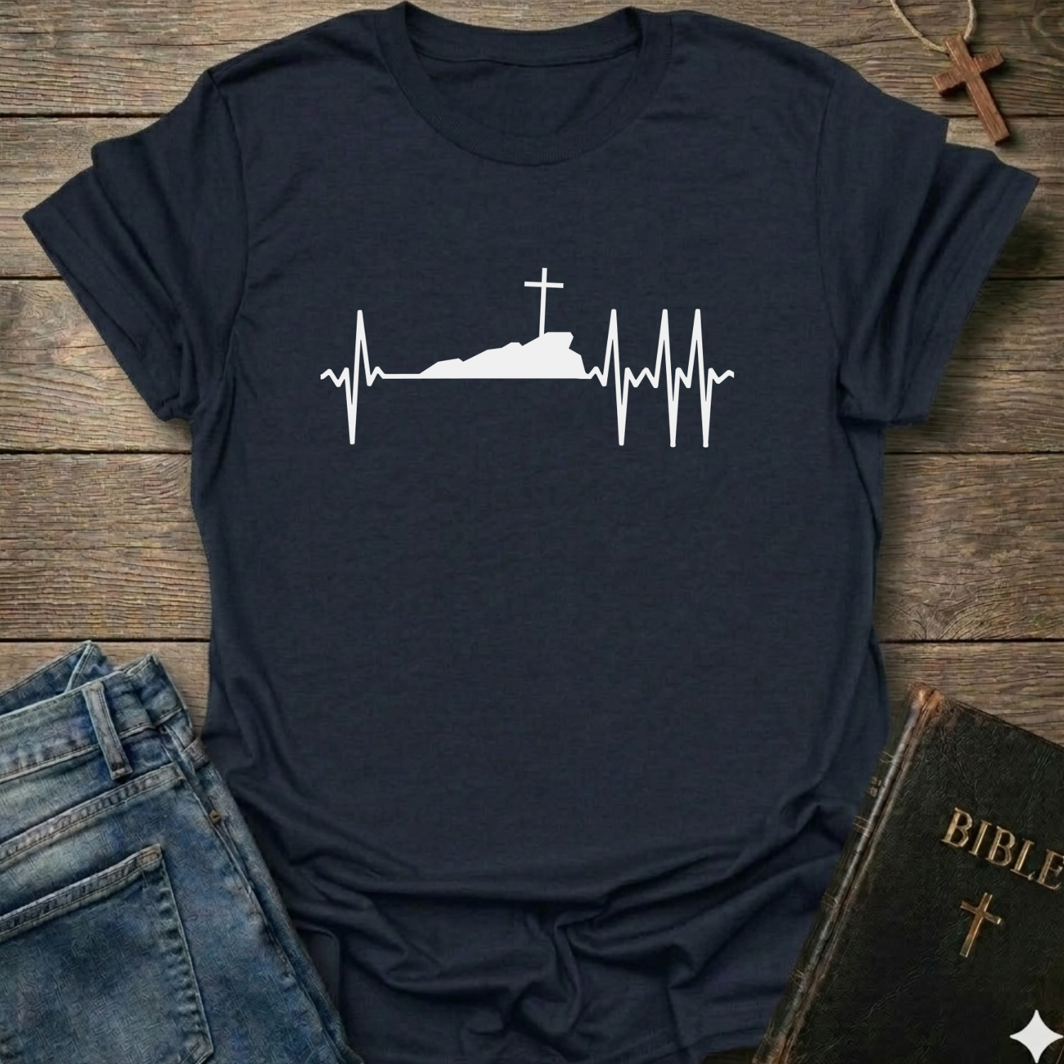 Navy blue T-shirt with a white graphic design Cross Heartbeat Lifeline Christian minimal faith apparel conversation starter on a wooden surface with jeans and a Bible.