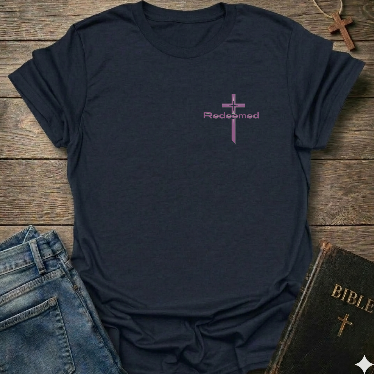 Navy t-shirt with a purple cross and 'Redeemed' text Christian minimal faith apparel Faith Forward on a wooden surface with jeans and a Bible.