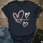 Navy blue t-shirt with 'Forgiven' text and pink hearts on a wooden surface with jeans and a Bible. Forgiven Christian T-Shirt 1 John 1:9 bold faith apparel Faith Forward women