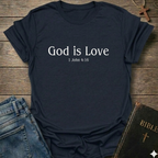 Navy blue with 'God is Love'  Christian T-Shirt 1 John 4:15 elegant faith apparel Faith Forward text. T-shirt on a wooden surface with jeans and a Bible.