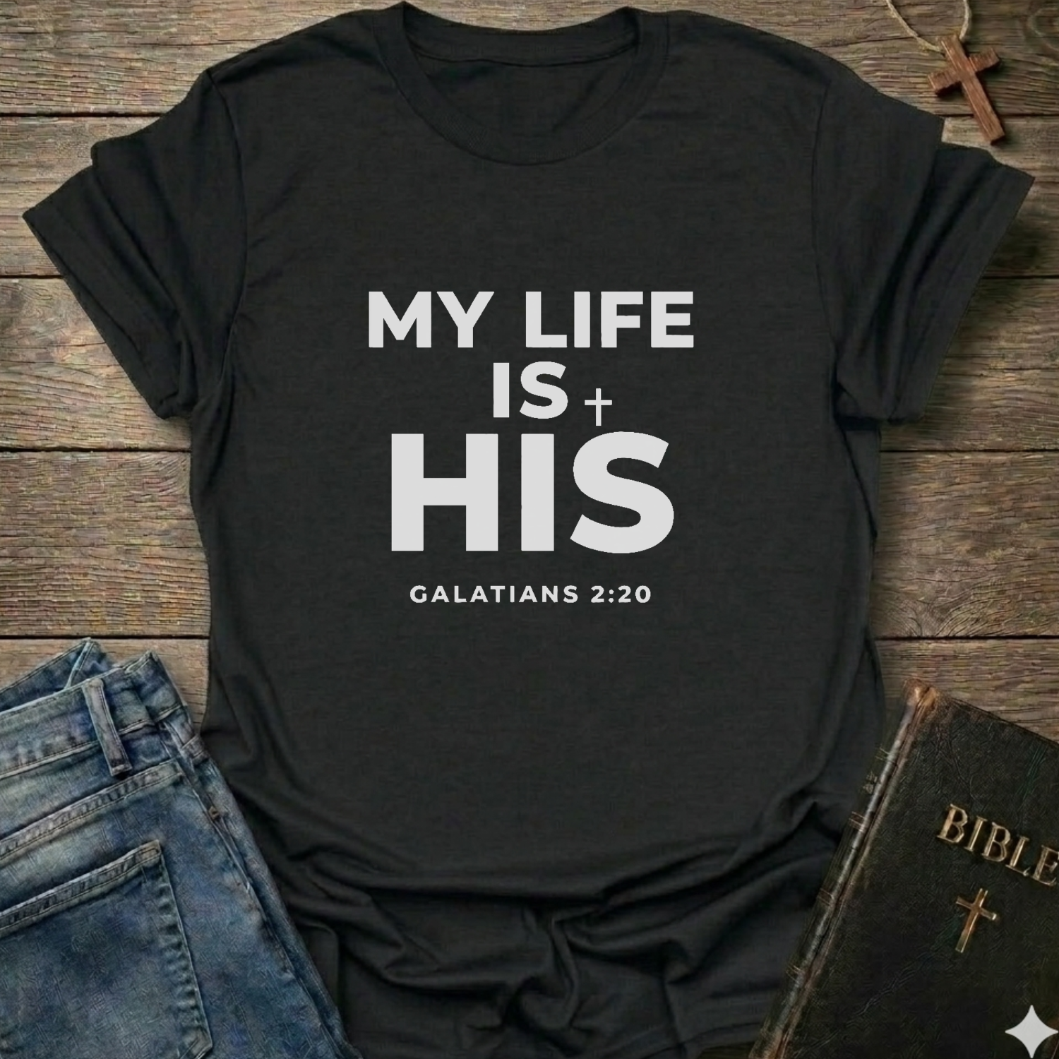 Black t-shirt with 'My Life Is His'  Christian T-Shirt Galatians 2:20 bold faith apparel Faith Forward text on a wooden surface with jeans and a Bible.