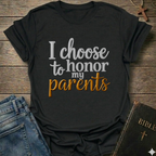 Black t-shirt with 'I choose to honor my parents' Exodus 20:12 text navy gold Christian faith apparel conversation starter. T-shirt is on a wooden surface with jeans and a Bible.