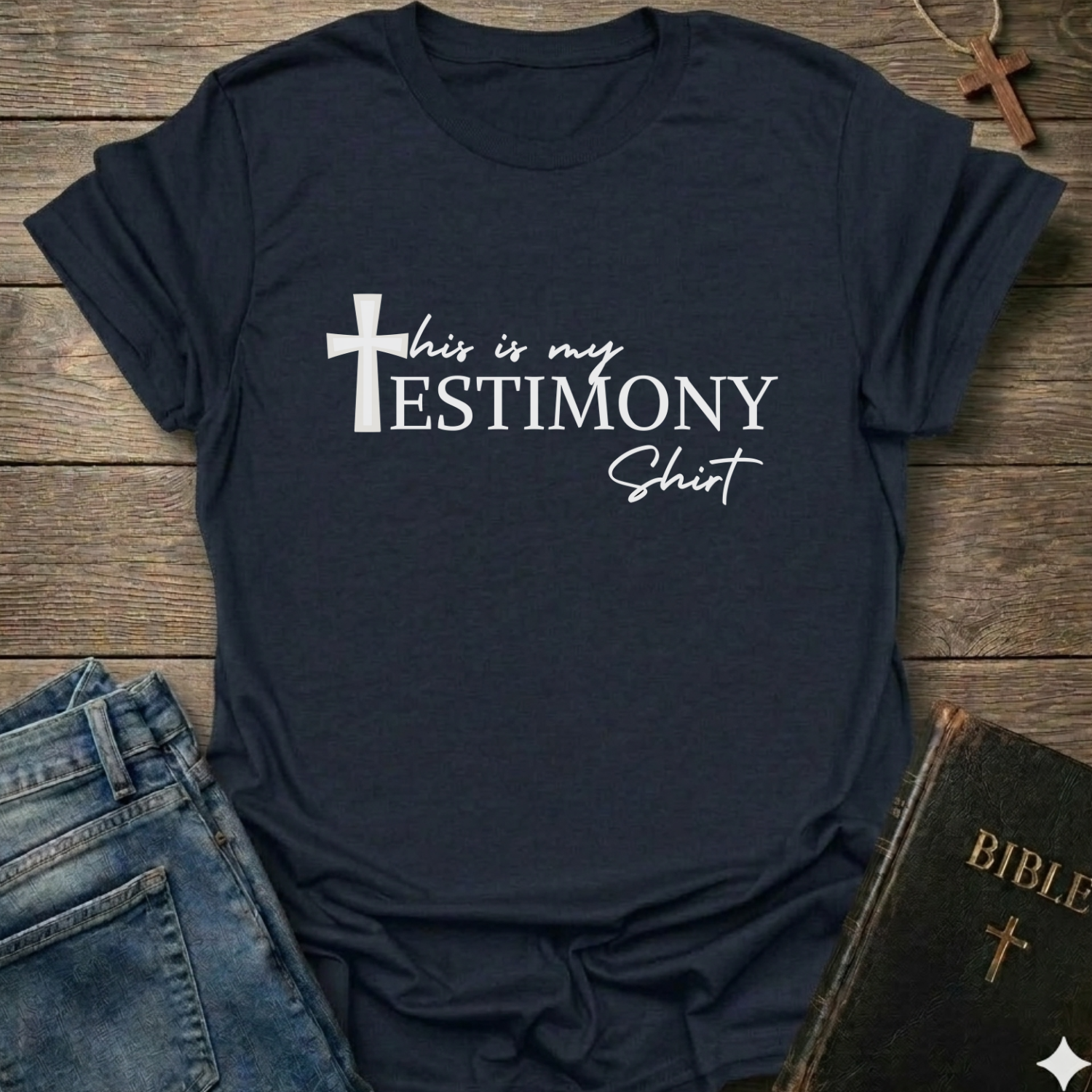Navy blue t-shirt with 'This is my testimony shirt' text and cross minimal faith apparel conversation starter. It is on a wooden surface with jeans and a Bible.