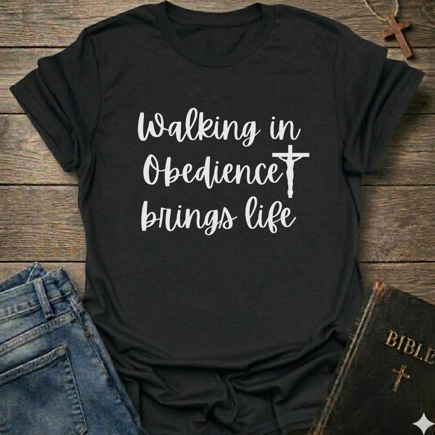 Black t-shirt with 'Walking in Obedience brings life' text and cross graphic Christian script faith apparel conversation starter on a wooden surface.