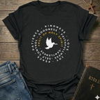 A black short-sleeve graphic T-shirt laid flat on a rustic wooden surface, styled with blue jeans, a Bible, and a wooden cross. The shirt features a circular white and yellow print with a dove in the center and words including 'PATIENCE', 'KINDNESS', 'GOODNESS', 'FAITH', 'LOVE', 'JOY', 'PEACE', and 'GENTLENESS', with 'FRUIT OF HOLY SPIRIT' in yellow.