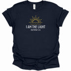 A navy blue short-sleeve t-shirt with a graphic on the chest featuring a yellow sun and the text 'I AM THE LIGHT MATTHEW 5:14' in white, displayed on a clean white background.