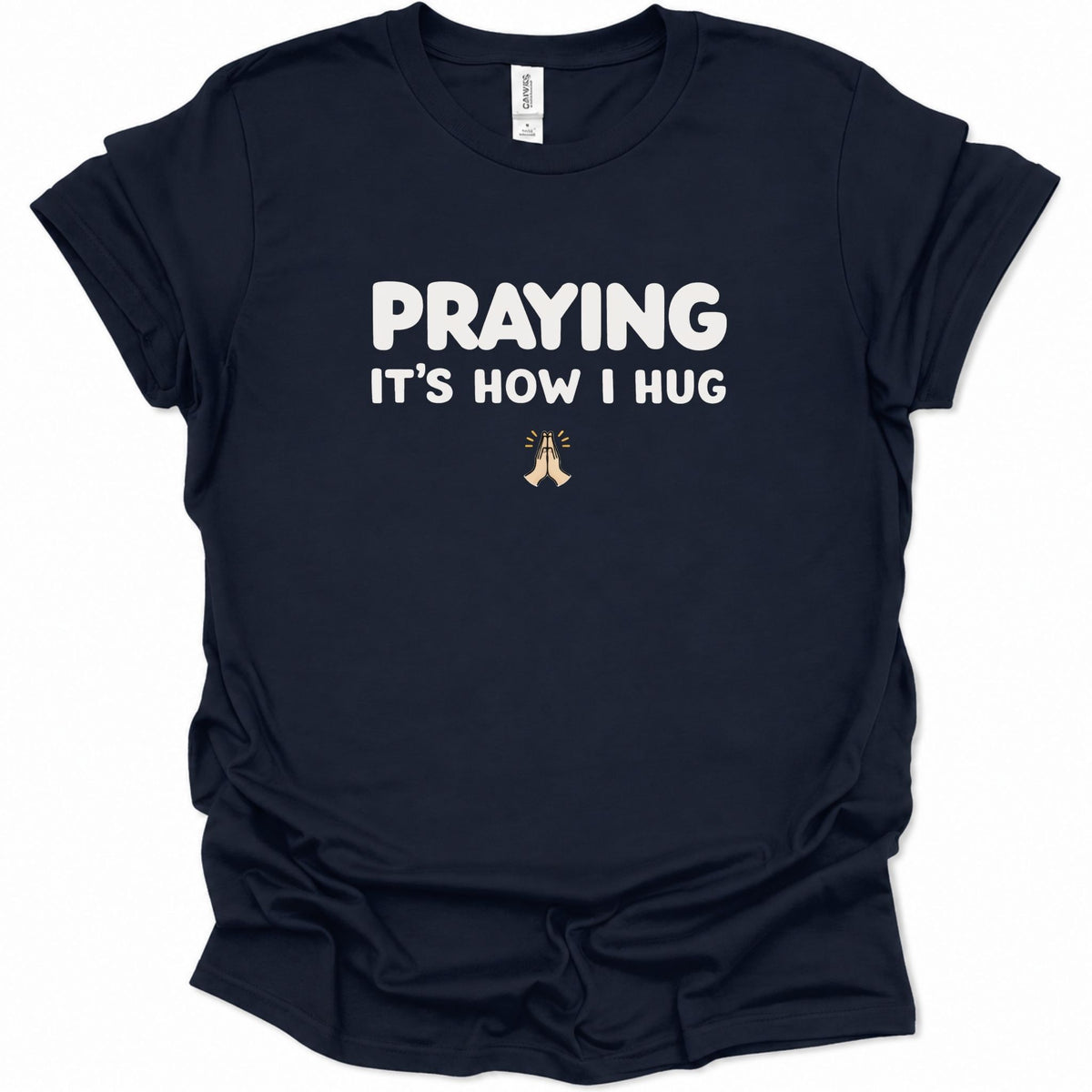 A navy blue short-sleeve t-shirt with white text reading 'PRAYING IT'S HOW I HUG' and a small praying hands graphic below, shown on a plain white background.