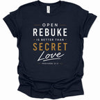 A navy blue short-sleeve t-shirt with a graphic print on the front reading 'OPEN REBUKE IS BETTER THAN SECRET Love' and 'PROVERBS 27:5' in white and gold lettering, shown on a plain white background.