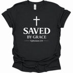 A black short-sleeve crewneck t-shirt with a distressed white graphic print on the front featuring a cross, the word 'SAVED', 'BY GRACE', and the Bible verse 'Ephesians 2:8'.