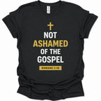 A black short-sleeve t-shirt with a graphic print on the front. The print features a gold cross above the text 'NOT ASHAMED OF THE GOSPEL' in white and gold lettering, and a gold box at the bottom reading 'ROMANS 1:16'.