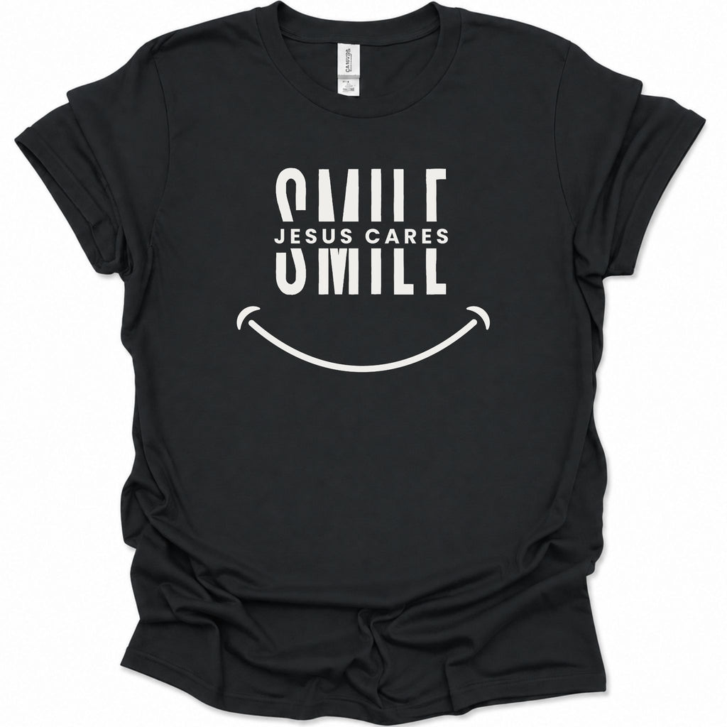 A black short-sleeve t-shirt with a white graphic print that reads 'SMILE JESUS CARES SMILL' above a smiley face, shown on a plain white background.