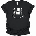 A black short-sleeve t-shirt with a white graphic print that reads 'SMILE JESUS CARES SMILL' above a smiley face, shown on a plain white background.