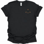 A black short-sleeve crewneck t-shirt with a small minimalist graphic on the left chest consisting of three brown dots and a brown cross, displayed on a clean white background.