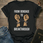 Black t-shirt with text 'From Bondage to Breakthrough' Christian T-Shirt and broken chains graphic faith apparel conversation starter
on a wooden surface.